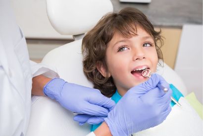 A smiling child in dentist chair having teeth examined with a mirror tool.