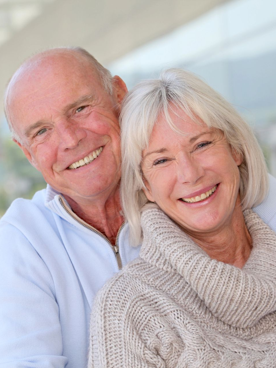 Smiling older couple, man with bald head, woman with blonde hair, close-up, outdoor setting.