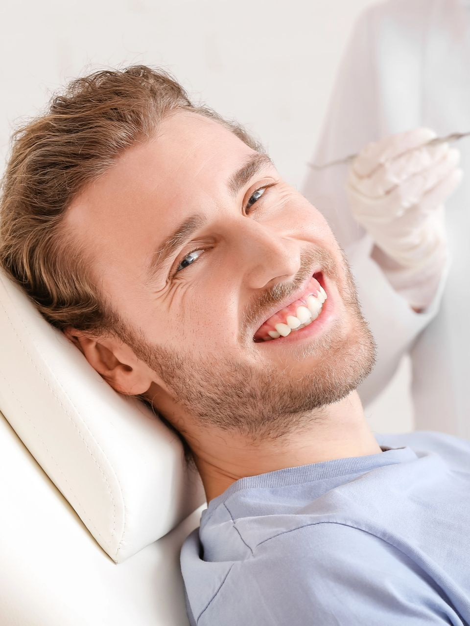 Man smiling in dental chair, dentist holding tool.