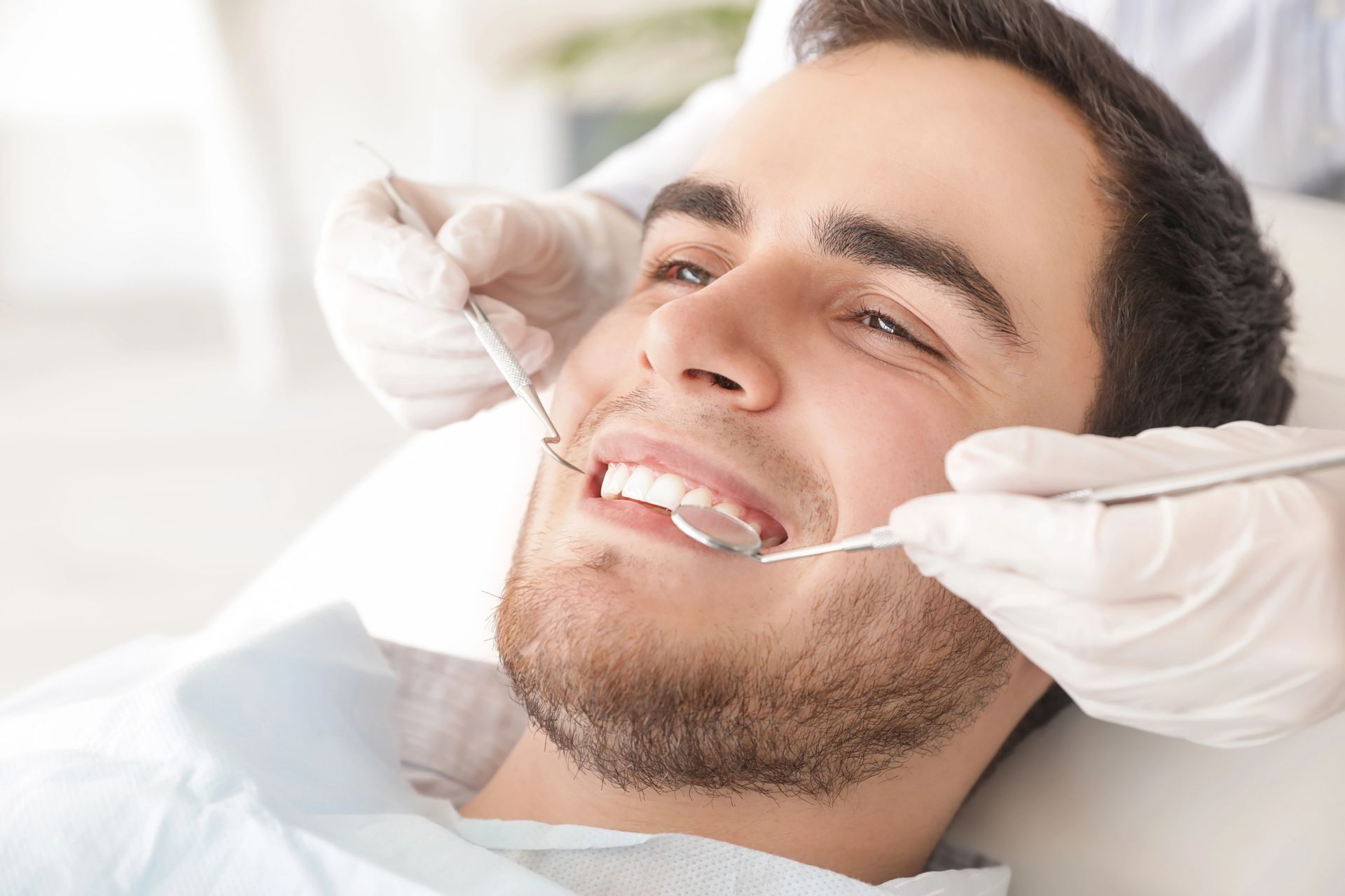 A person receiving a dental checkup. A dentist examines the person's teeth with dental tools in a bright office.