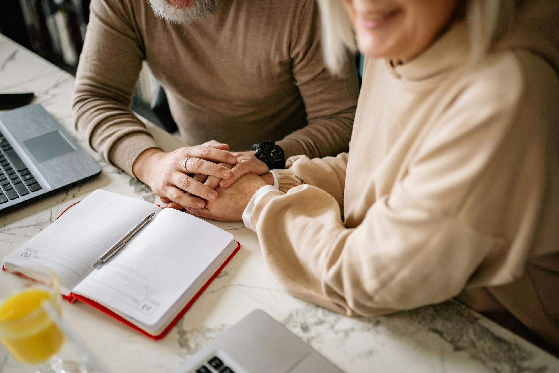 An elderly couple is sitting at a table with a laptop and a notebook.
