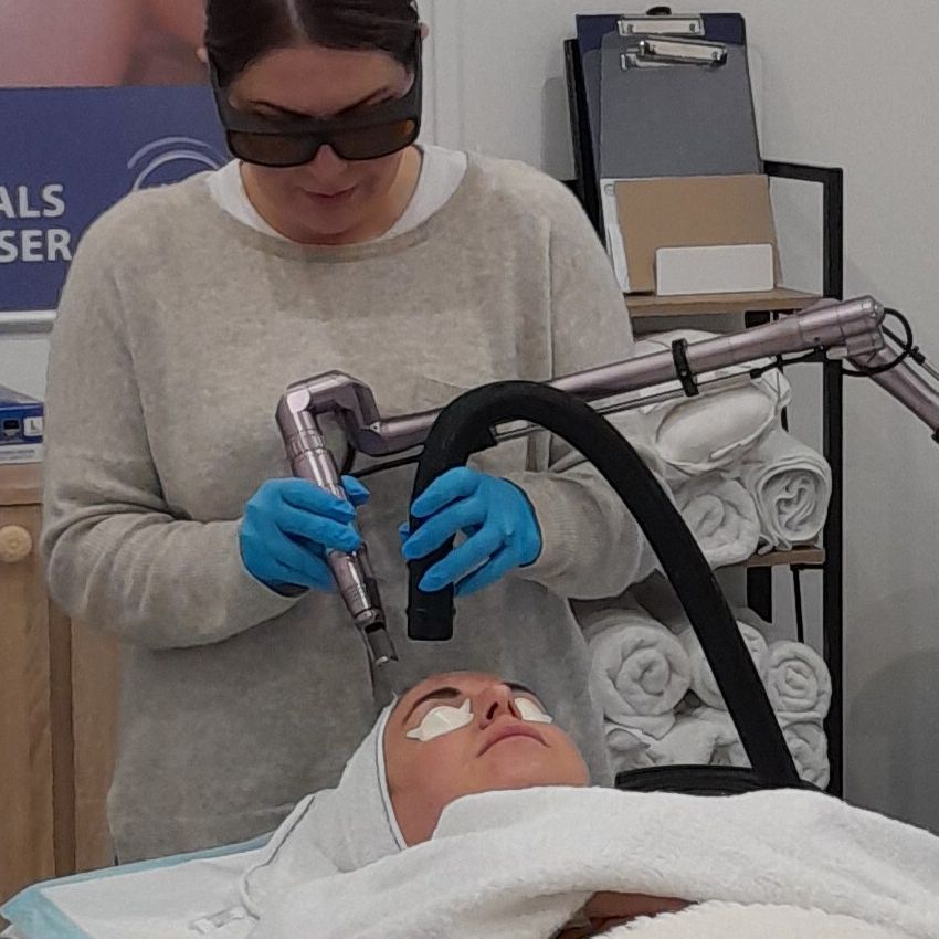 A woman wearing sunglasses is using a laser on a patient 's face