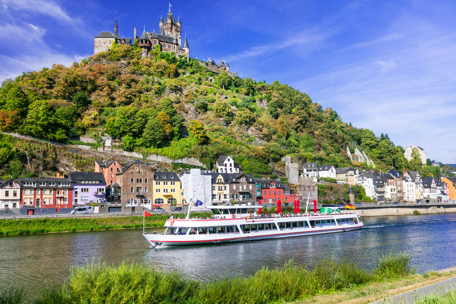 A boat is floating on a river in front of a castle on a hill.