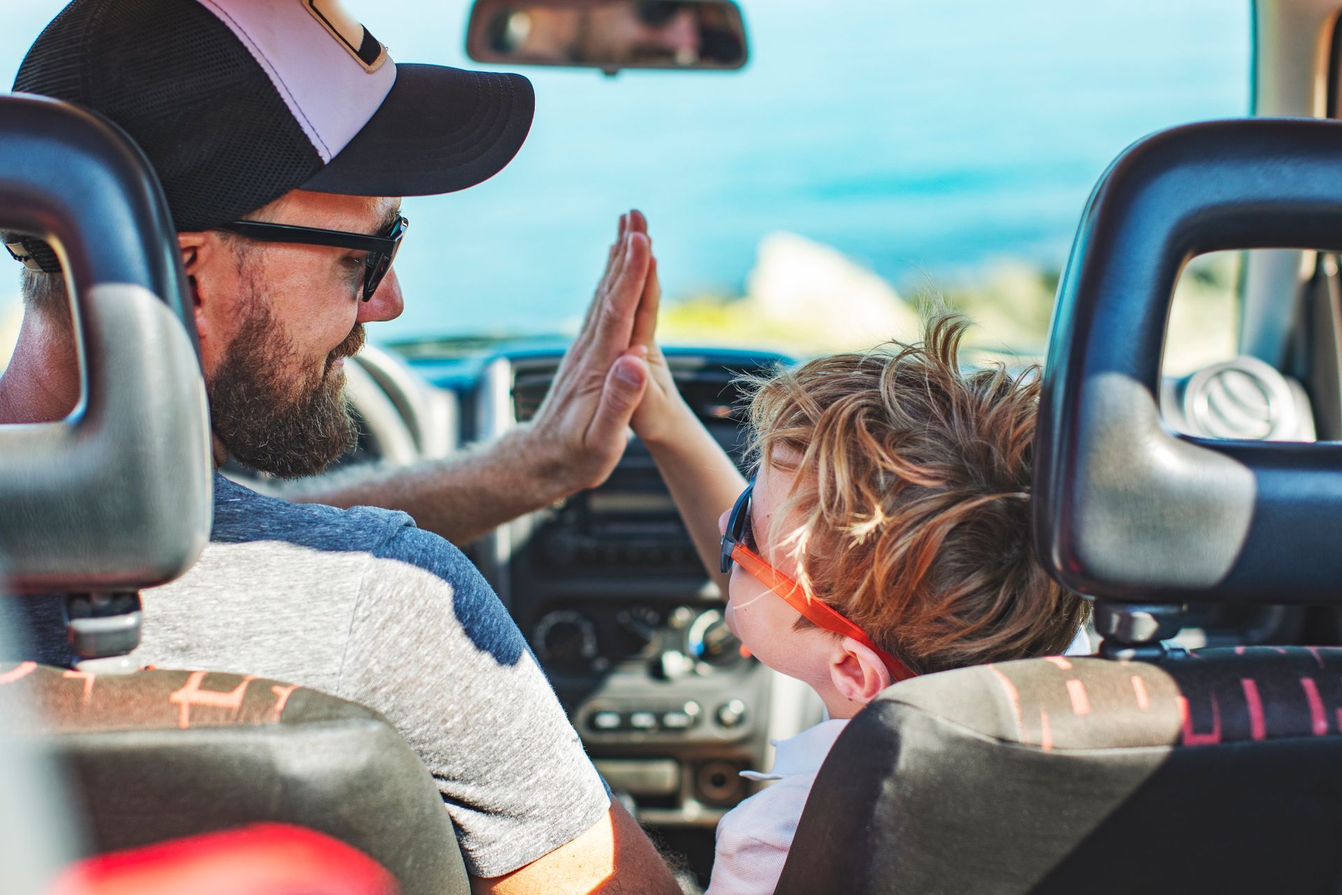A man and a child are giving each other a high five in a car.