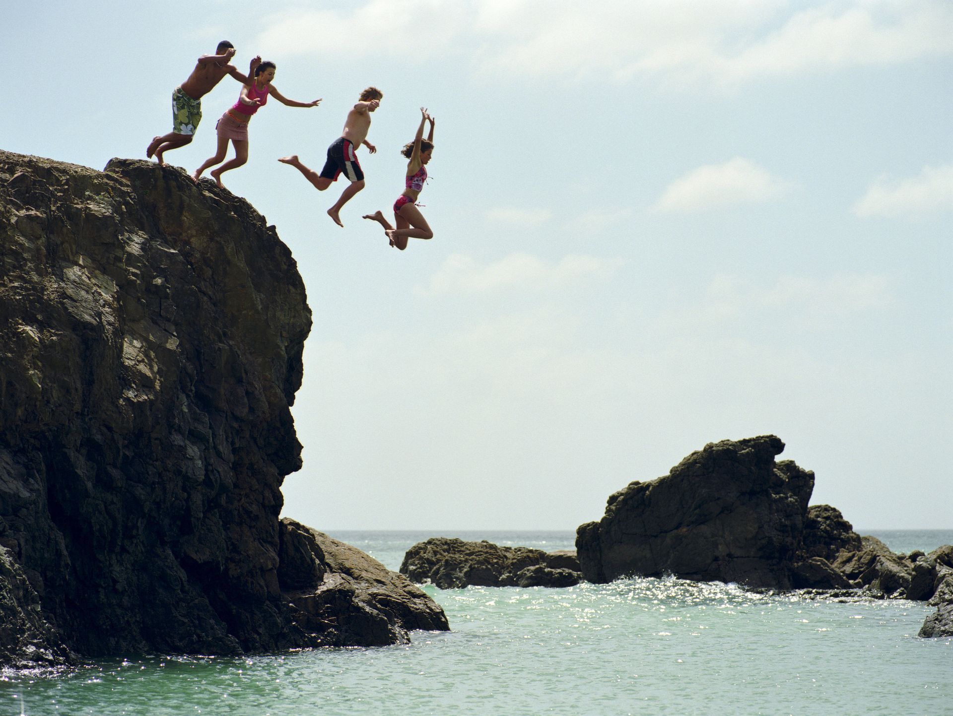 A group of people are jumping off a cliff into the ocean