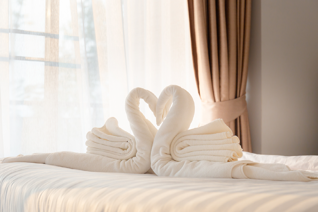 Two towels are folded into the shape of swans on a bed.