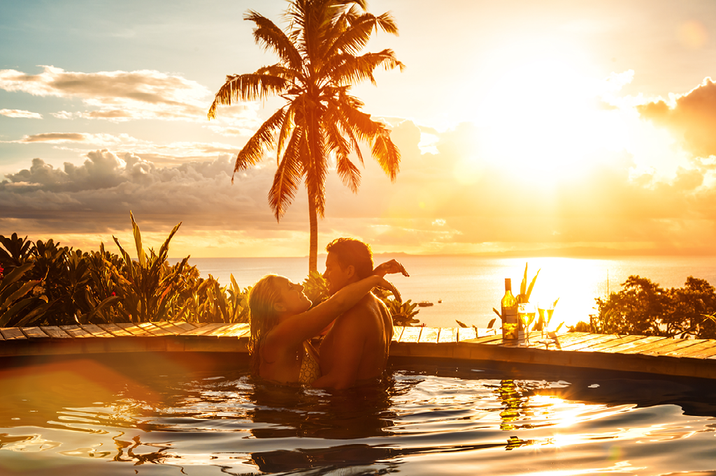 A man and a woman are kissing in a swimming pool at sunset.