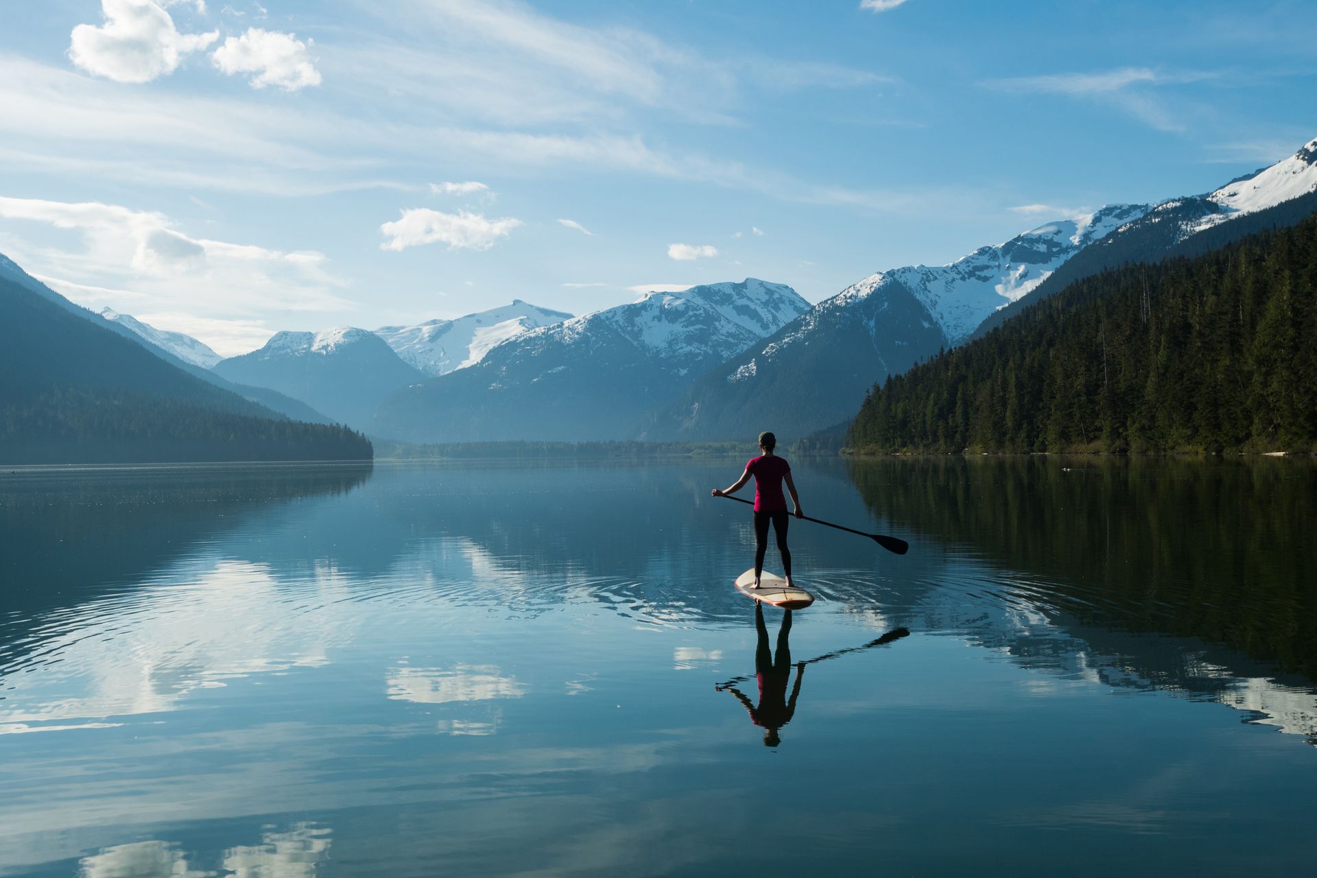 A man is riding a paddle board on a lake with mountains in the background.