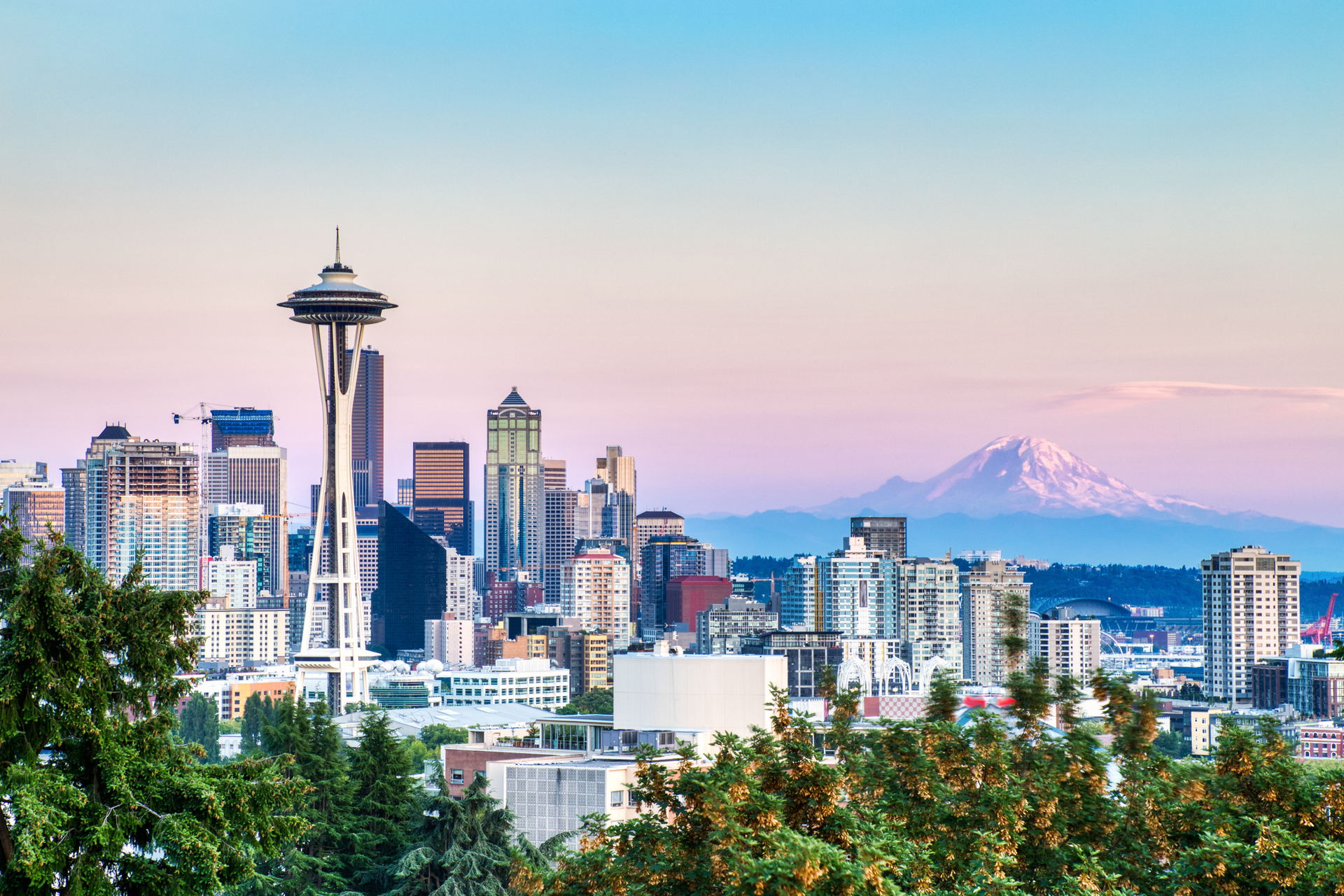 A city skyline with the space needle in the foreground and a mountain in the background.