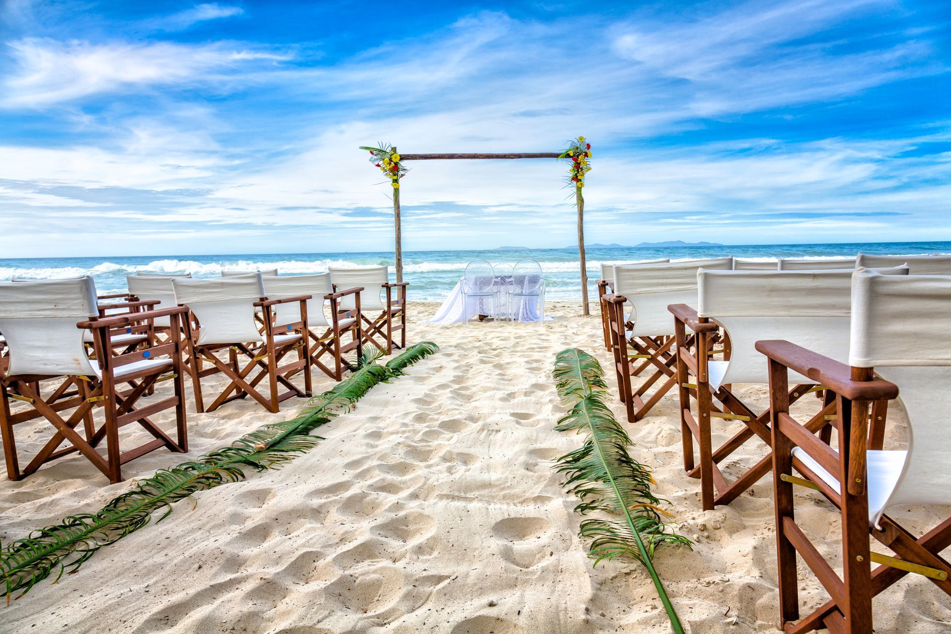 A row of folding chairs are lined up on a sandy beach.