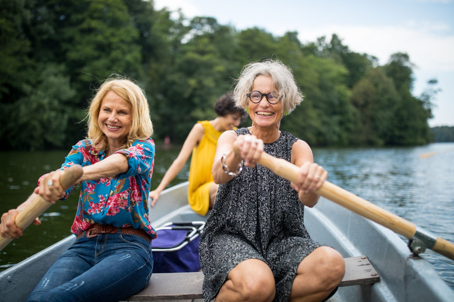 Three women are rowing a boat on a lake.