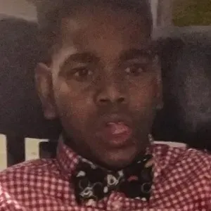 A young man wearing a bow tie and a plaid shirt is taking a selfie.