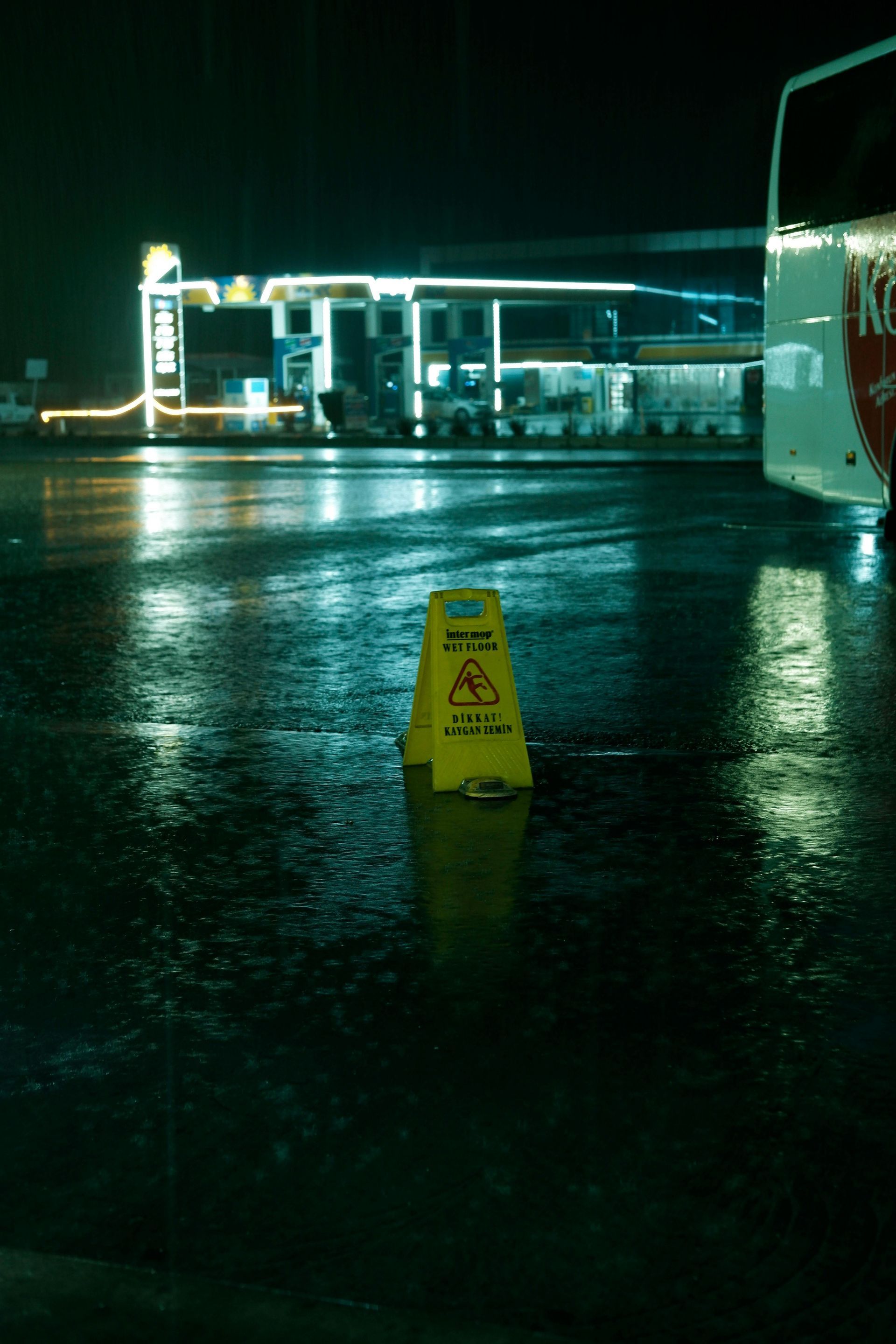 A yellow caution sign is sitting in a parking lot at night