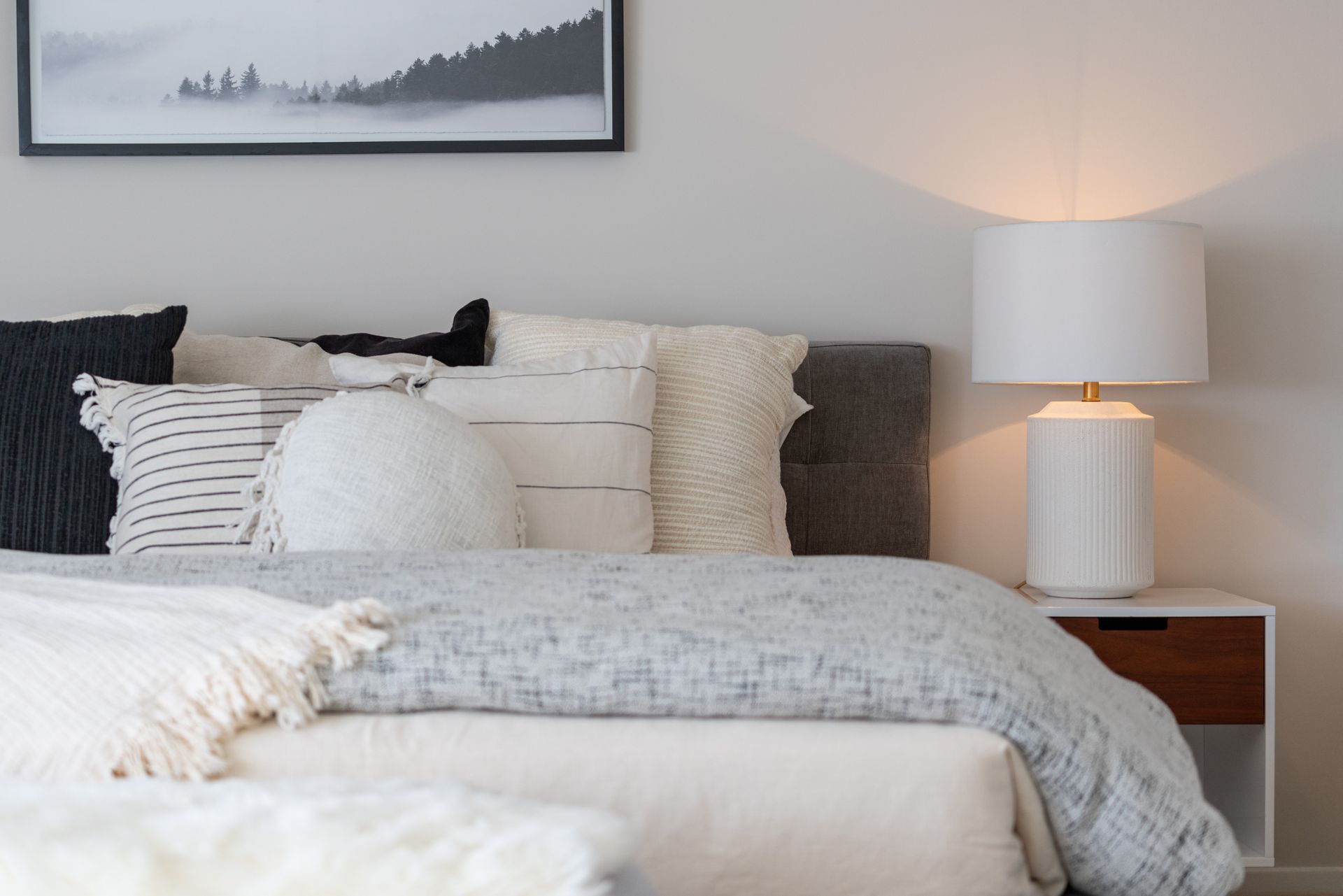 A bedroom with a bed , nightstand , lamp and picture on the wall.