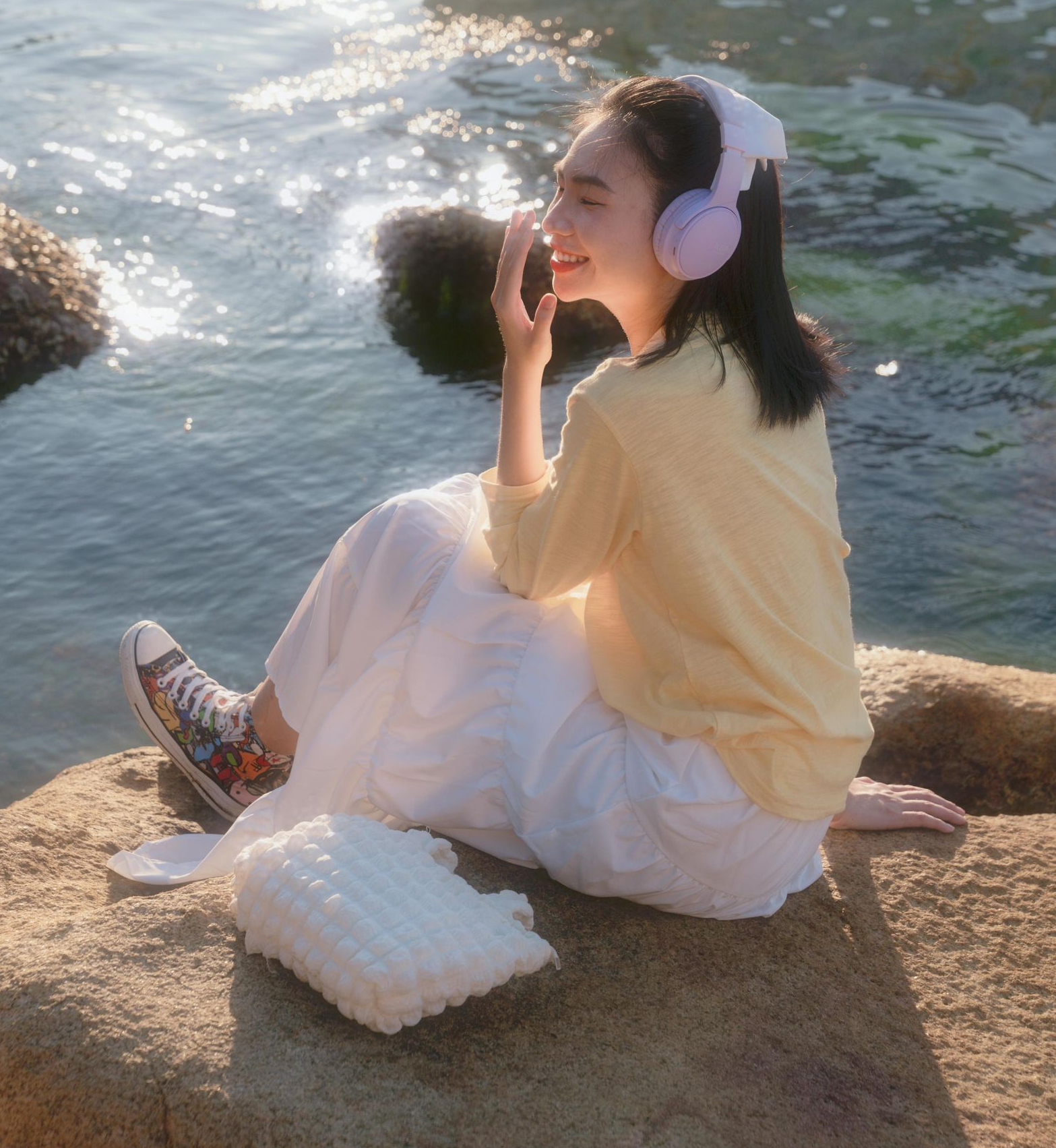 Woman sitting by the water listening to something on headphones.