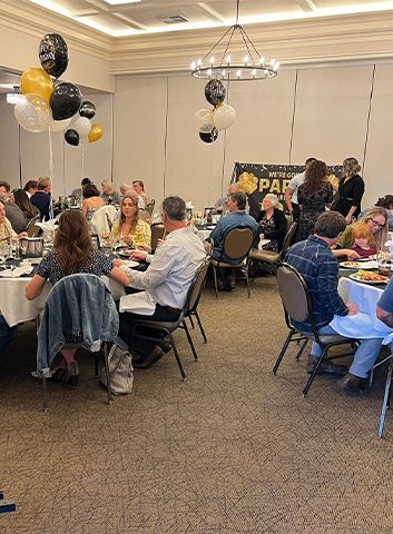 Event in a banquet hall with seated guests, decorated with balloons.
