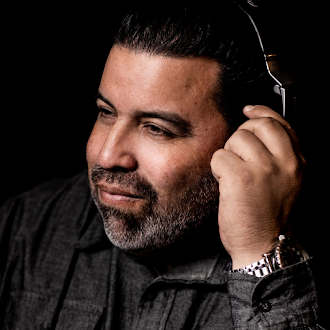 Man with a beard in a dark shirt, listening with headphones, looking contemplative.