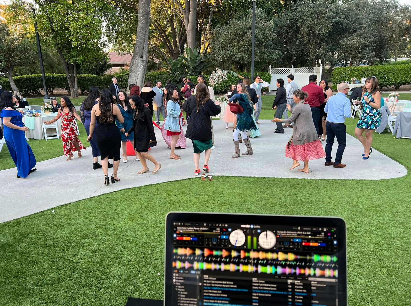 DJ setup with laptop playing music, people dancing outdoors on a stone patio.