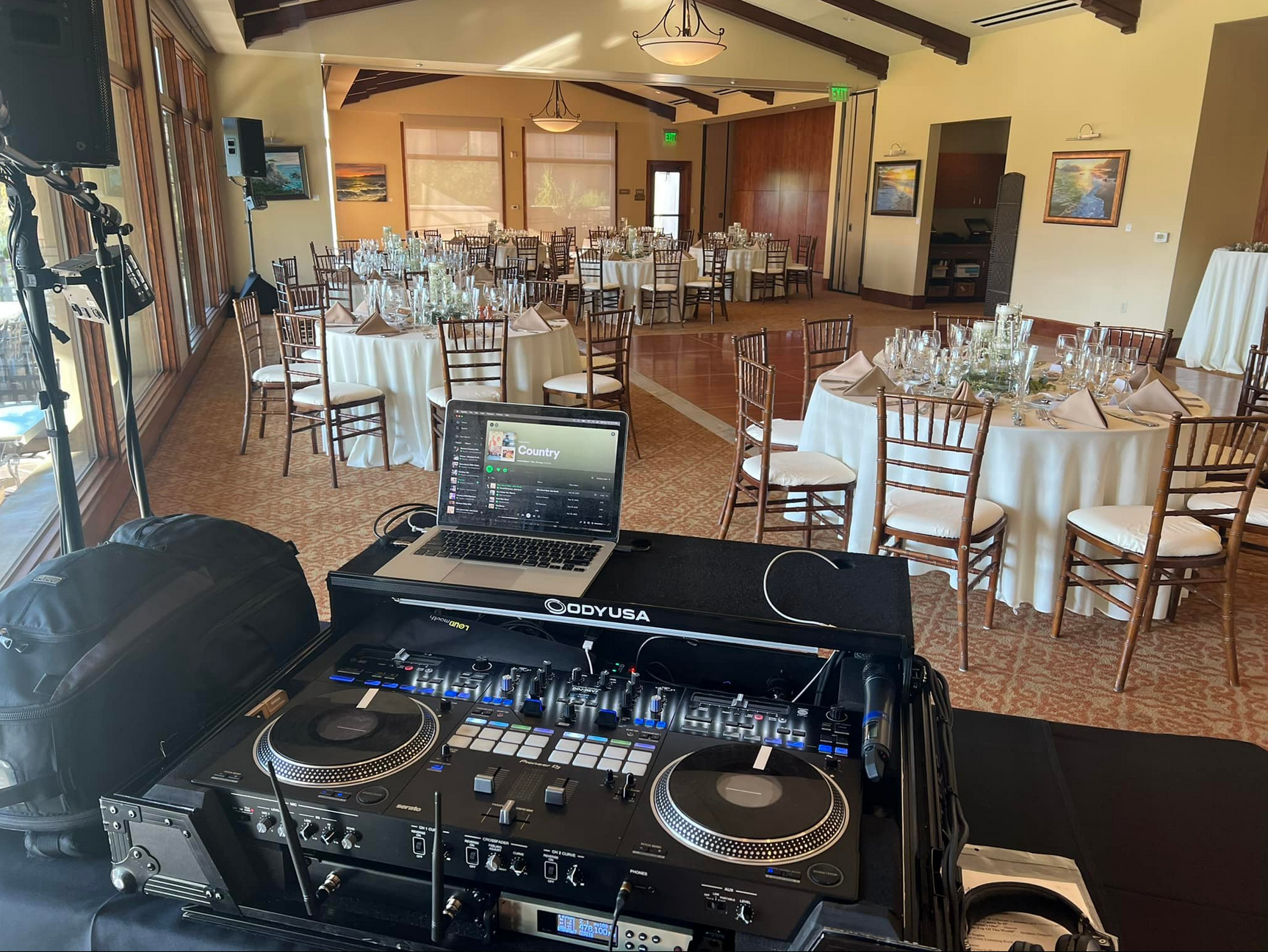 DJ setup at a wedding reception with tables set for guests in a large room.