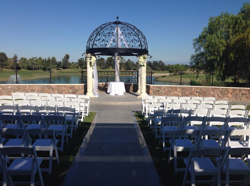 Wedding ceremony setup with white chairs facing a gazebo overlooking a lake on a sunny day.