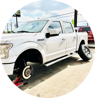 A white truck is sitting on a jack in a parking lot | Cordova Auto Center #4