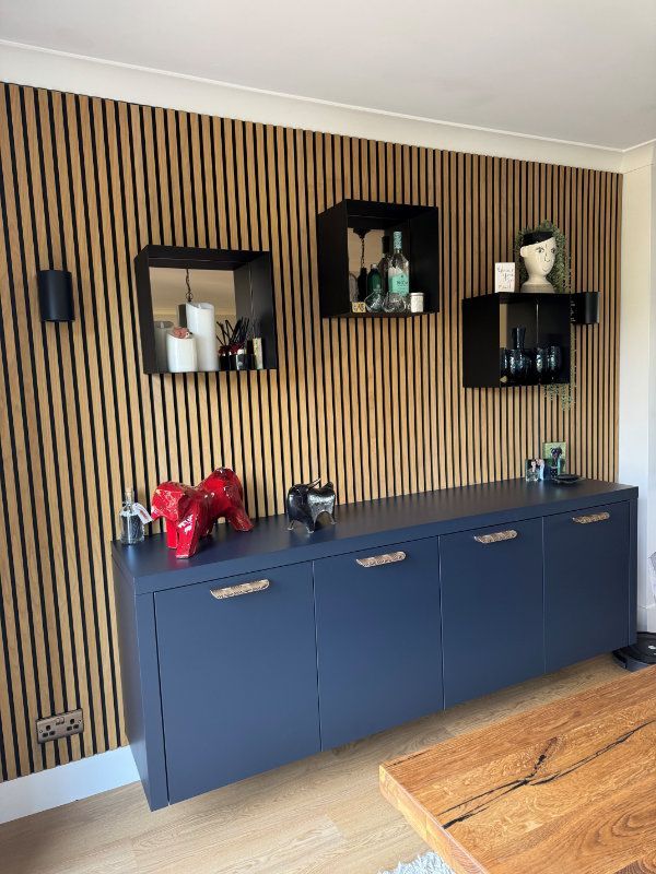 A living room with a striped wall , a dresser , a table and shelves.