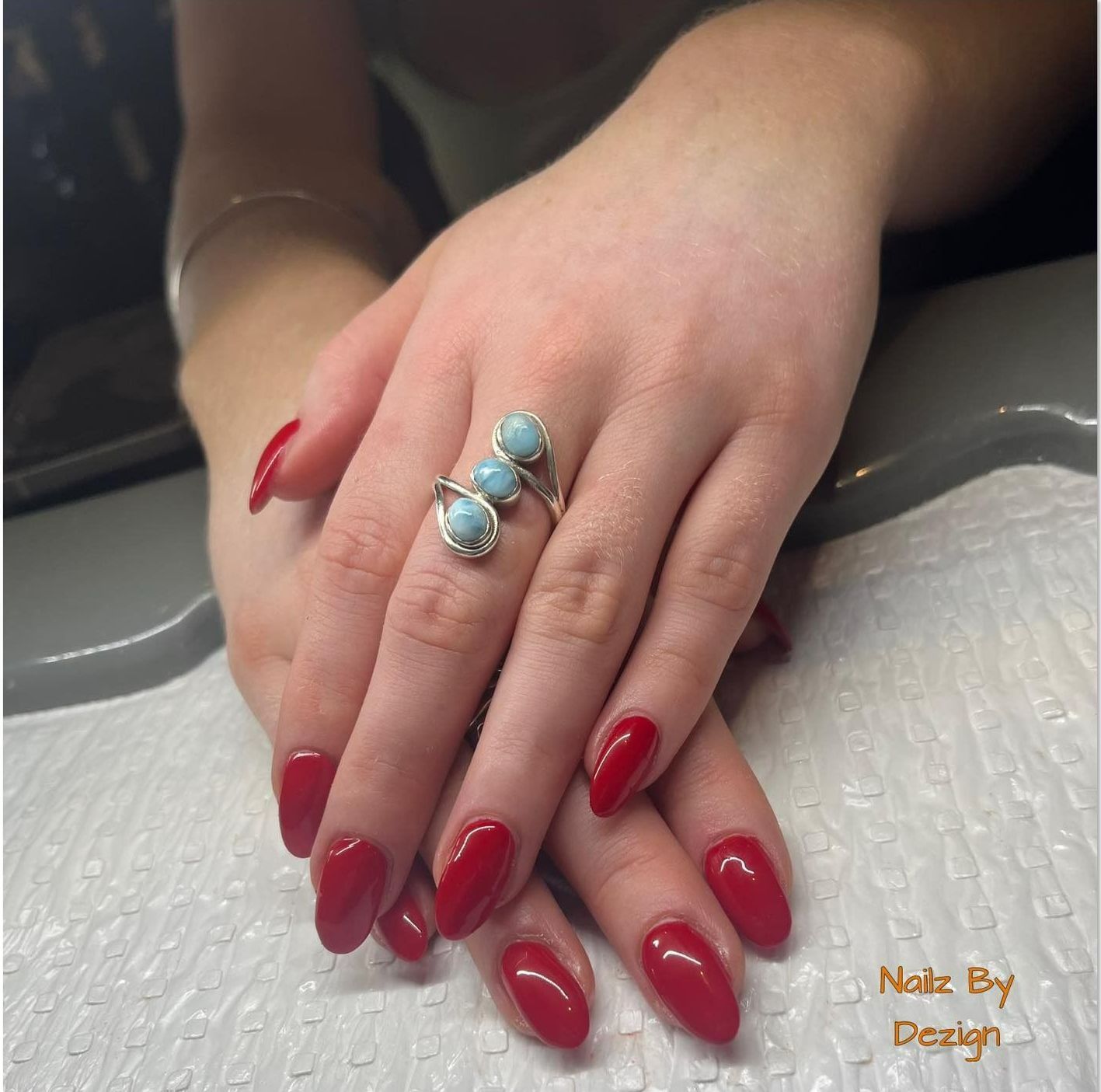A Woman's Hand With Red Nails and a Ring That Says Nails by Design — Nailz By Dezign In Airlie Beach, QLD