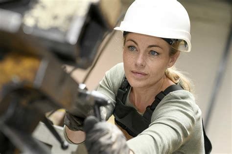 A woman wearing a hard hat and gloves is working on a machine.