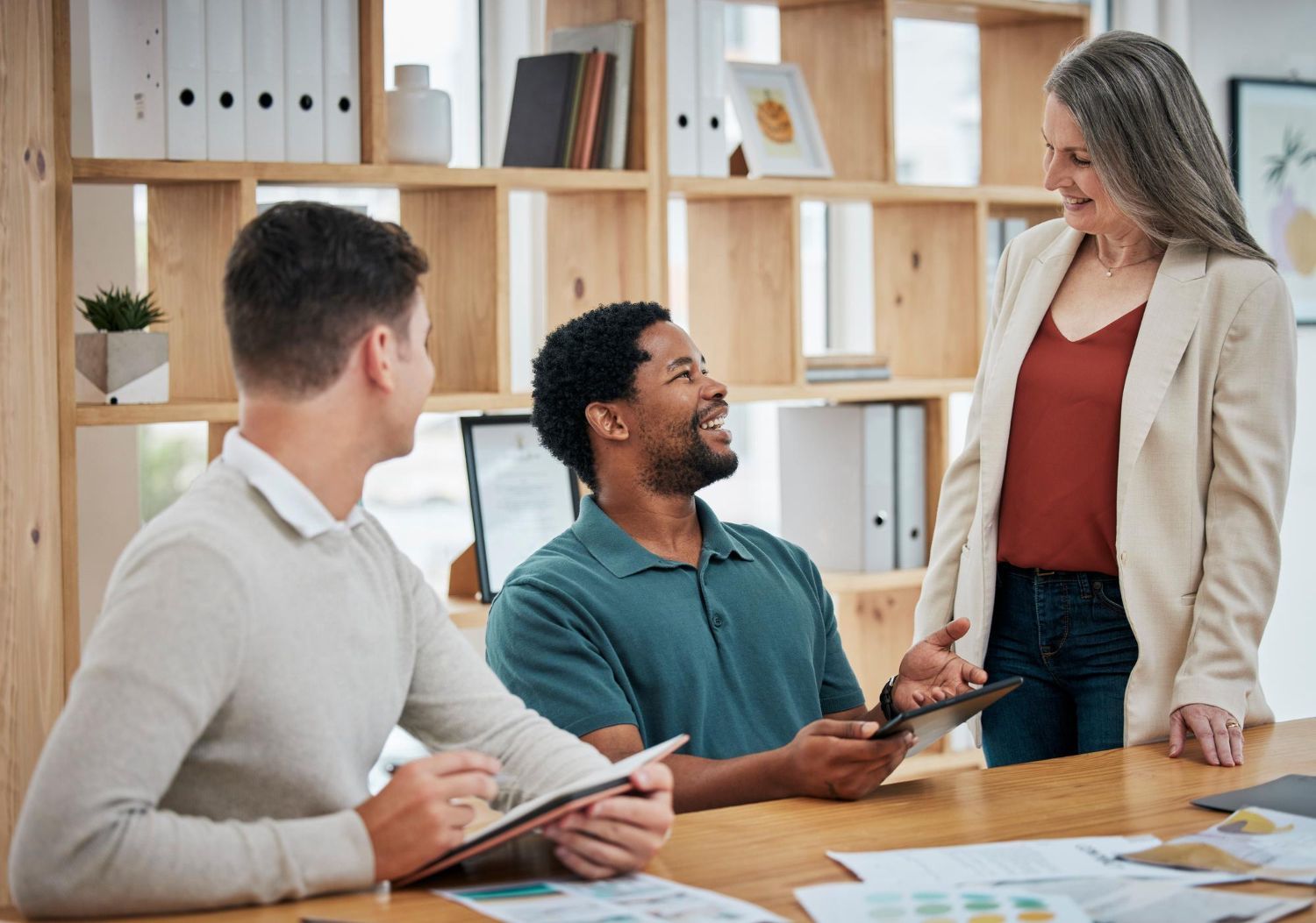 Three people in an office. A woman and two men, one holding a tablet. They appear to be in a meeting.