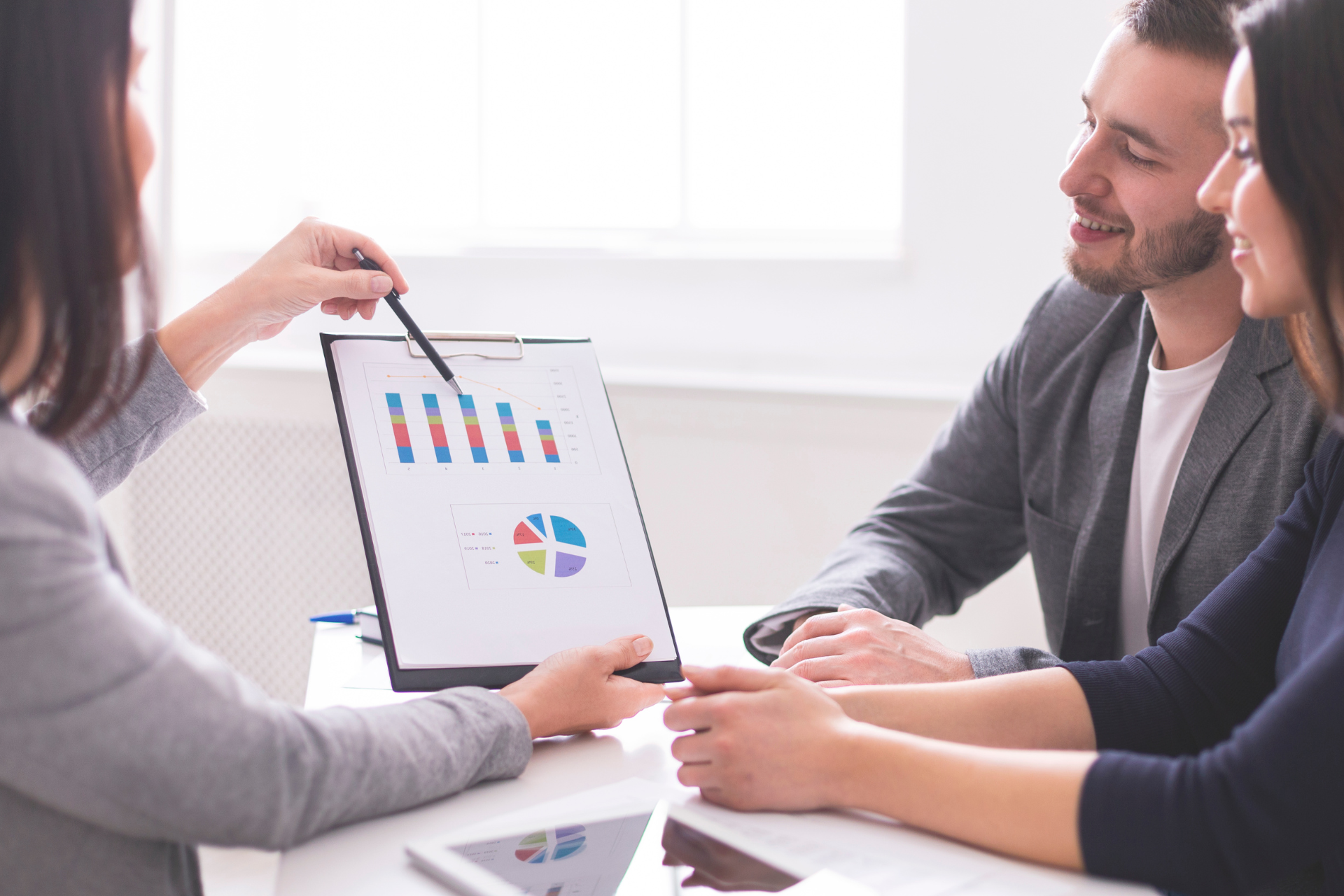 Woman pointing at charts, presenting to smiling couple at a table.