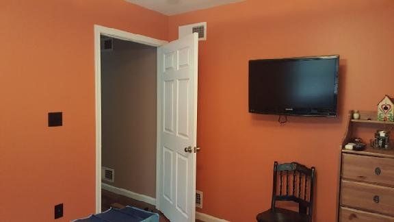 A bedroom with orange walls and a flat screen tv on the wall.