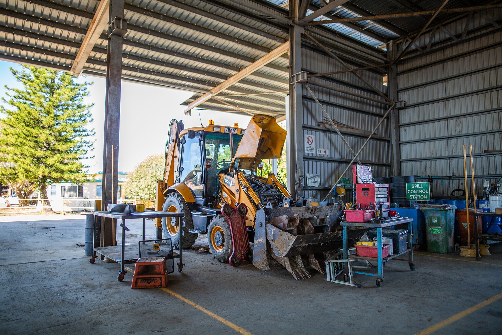 A yellow tractor is parked inside of a shed.
