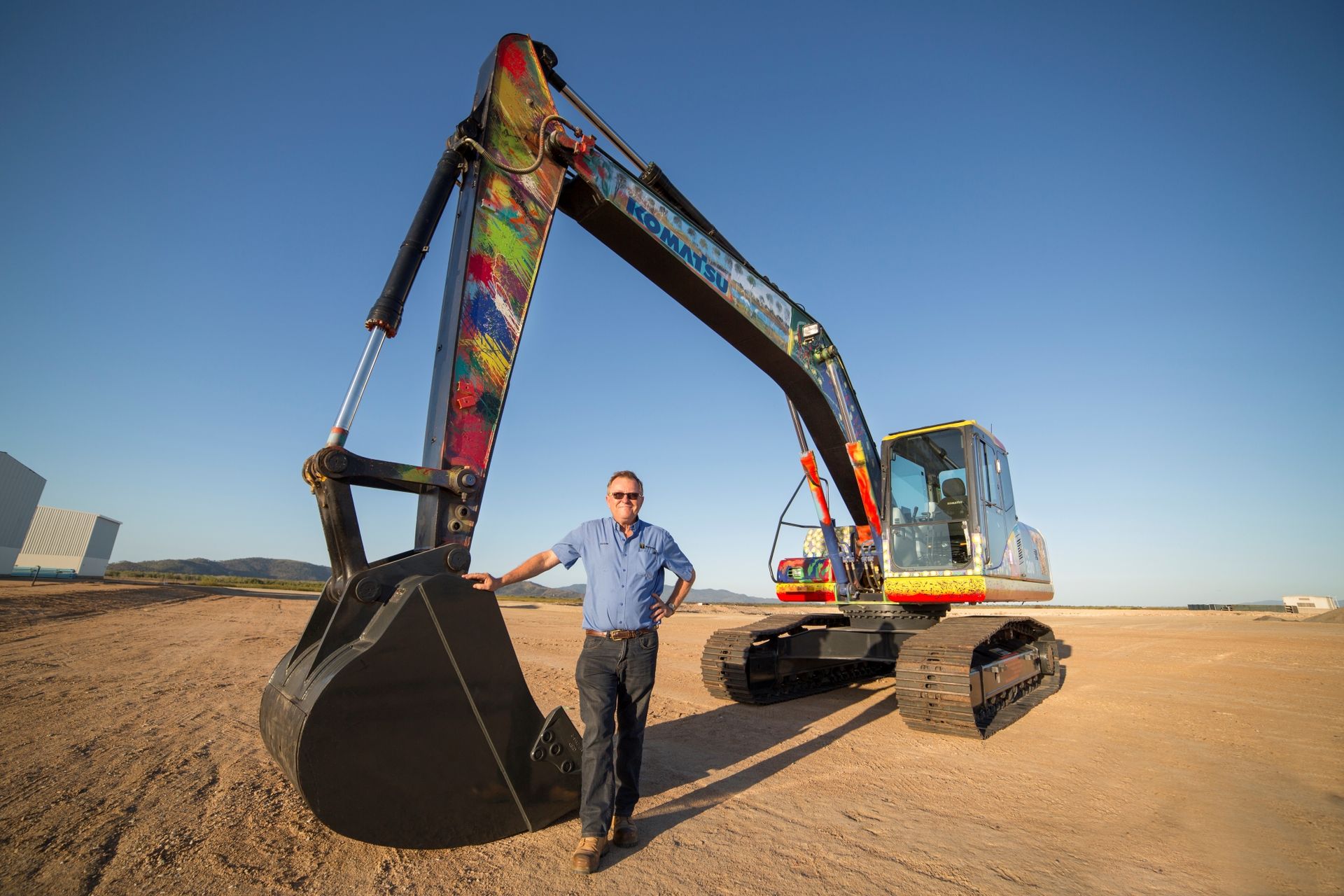 A yellow tractor is parked under a roof with its hood up.
