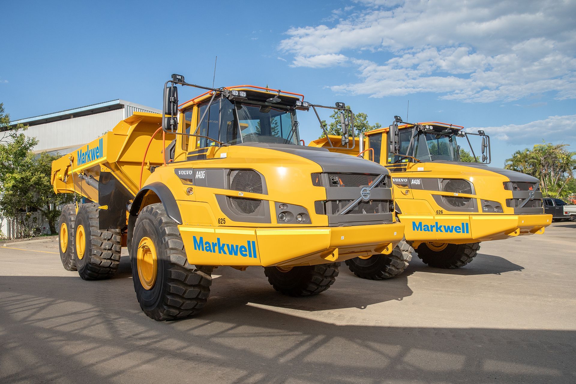 A man in a green shirt is standing next to a large excavator in a dirt field.