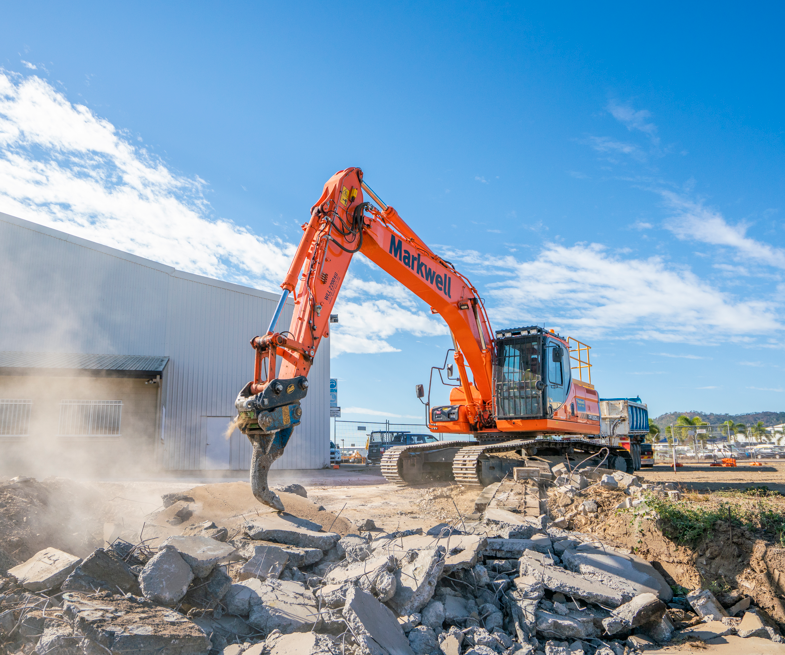 A large orange excavator is demolishing a building.