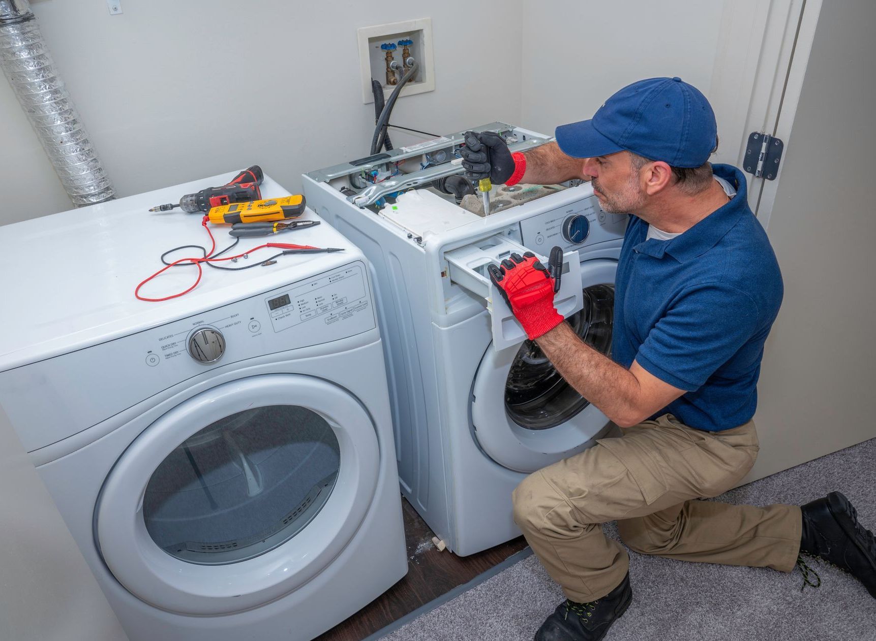 A man is fixing a washer and dryer in a laundry room.