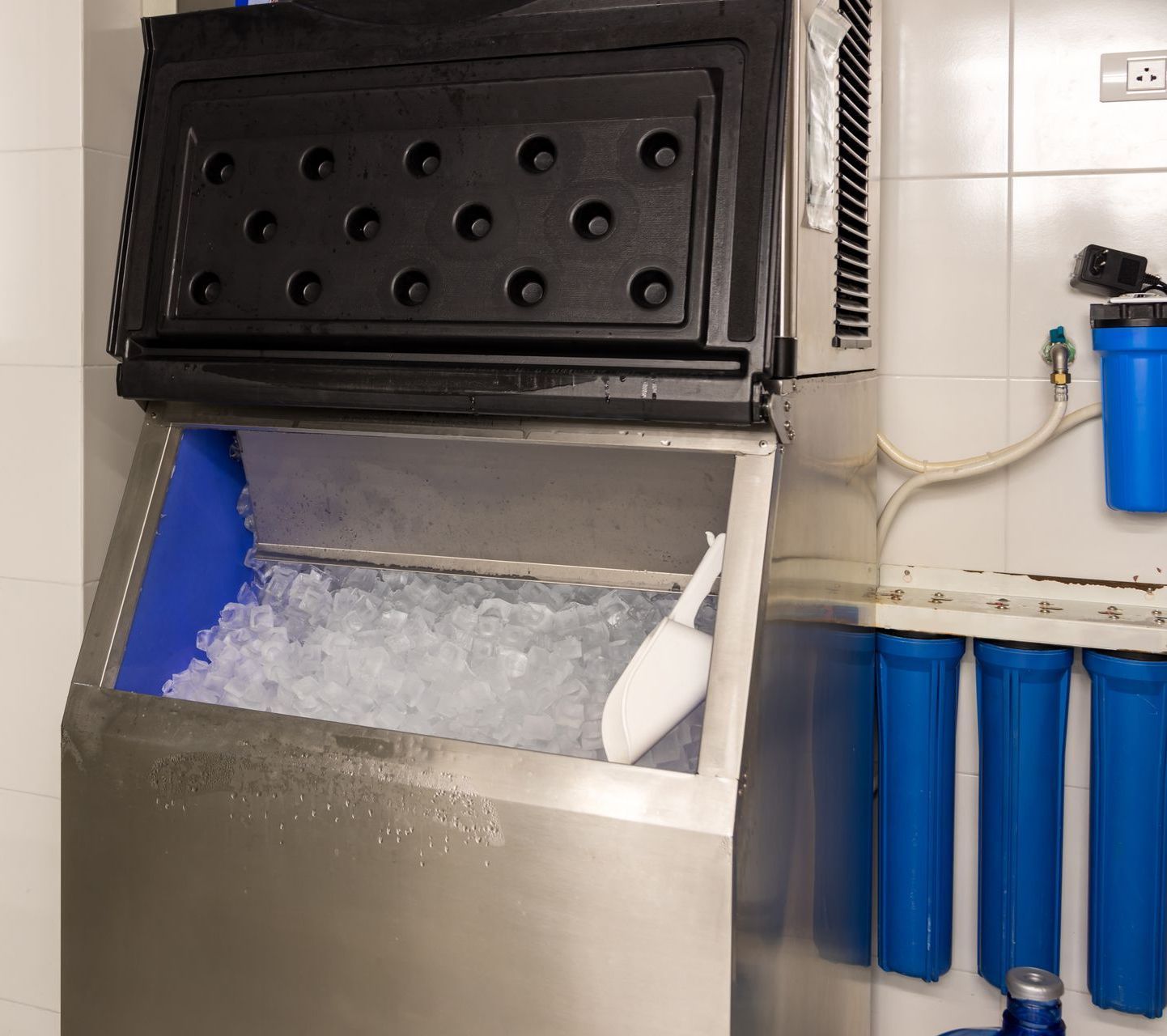 A stainless steel ice maker filled with ice and a scoop