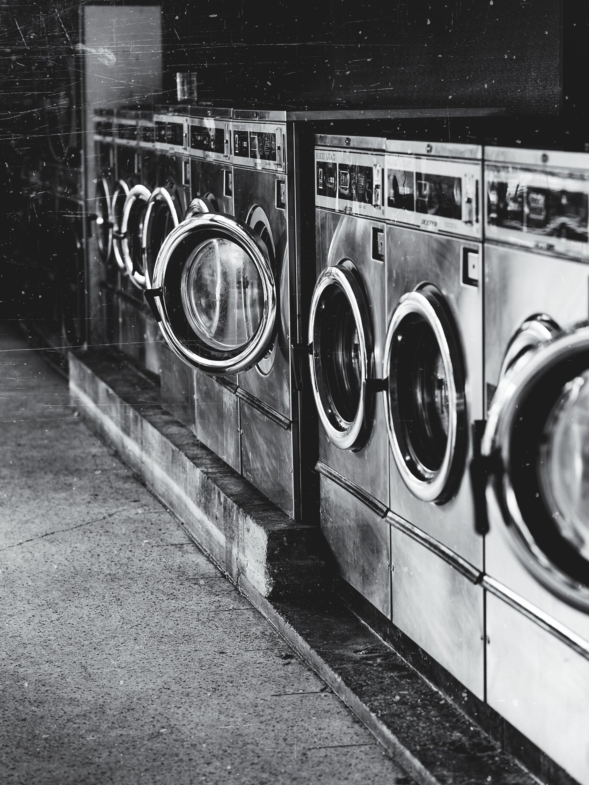 A black and white photo of a row of washing machines in a laundromat