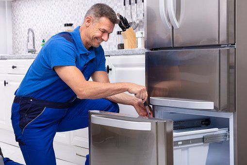 A man is fixing a refrigerator in a kitchen.