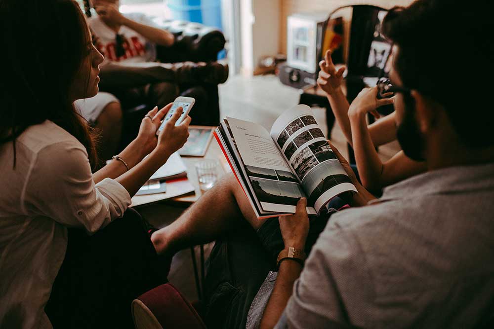 A group of people are sitting around a table reading magazines.