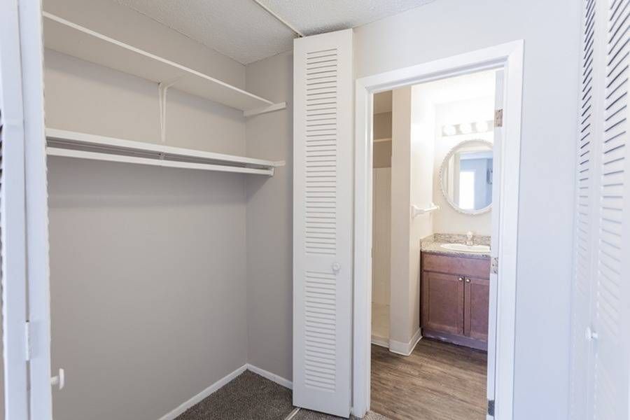 Walk-in closet with white shelves and doorway to a bathroom vanity.