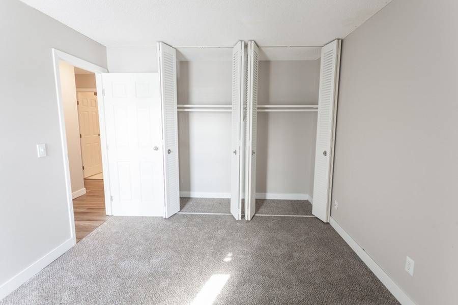 Bedroom with neutral walls, carpet, and an open double-door closet.