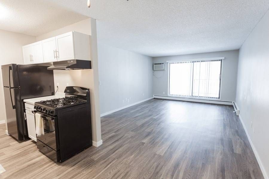 Open-concept kitchen with black refrigerator and stove, adjacent to a bright living area with a large window.