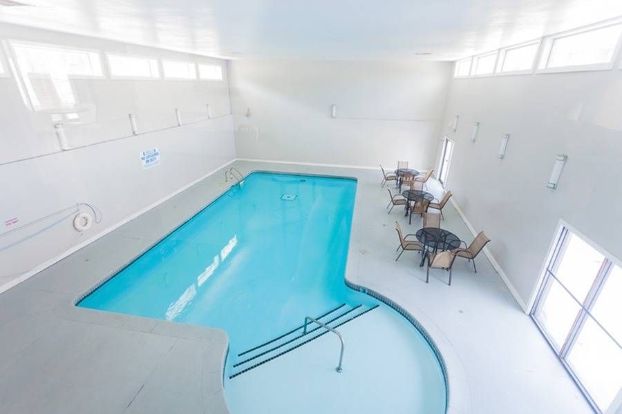 Indoor pool in a bright white room with seating along the wall.