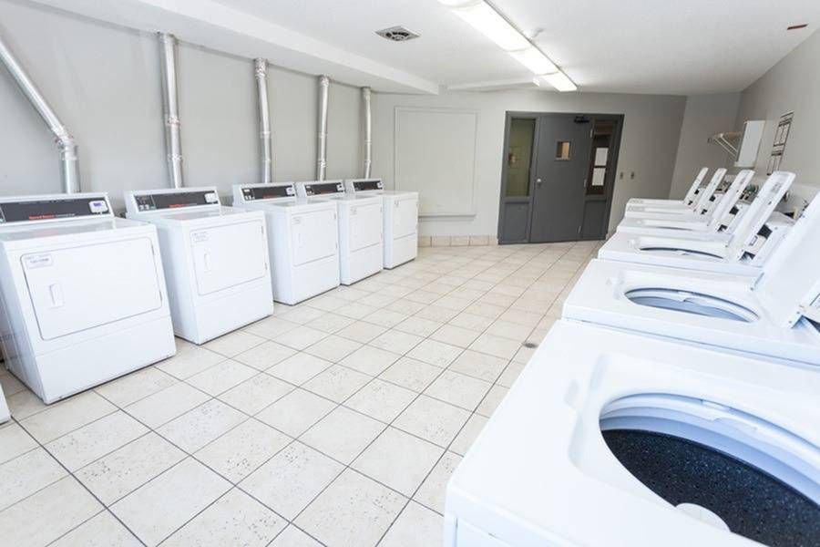 Shared laundry room with a row of washing machines and dryers along a tiled floor.