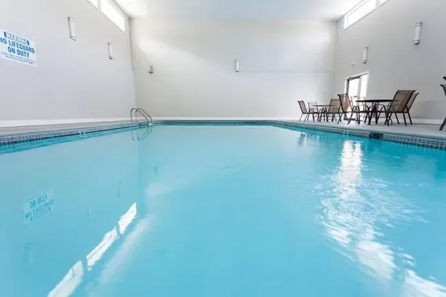 Indoor pool with clear water, blue tile, and seating area. White walls and ceiling with natural light.