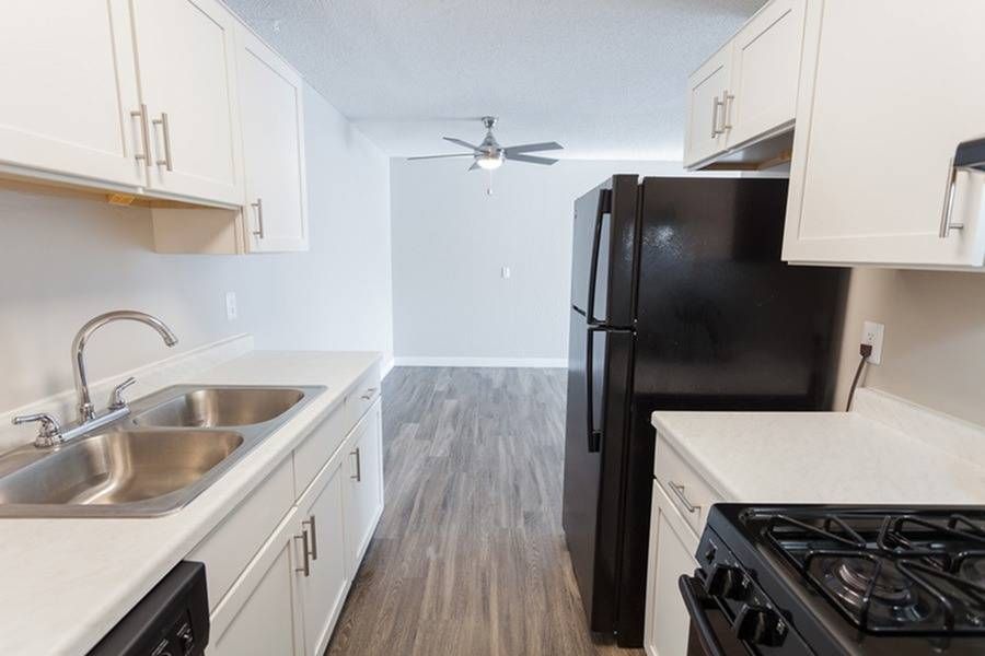 Bright modern kitchen with white cabinets, double stainless steel sink, and black refrigerator.