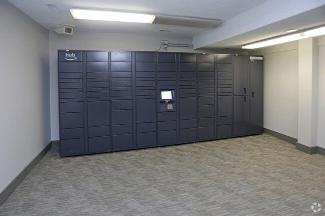 Dark gray parcel lockers in a room with light-colored walls and carpet. A touchscreen is in the center.