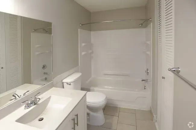 Bathroom with white fixtures: toilet, sink, bathtub. Gray walls, tile floor, large mirror, chrome hardware.