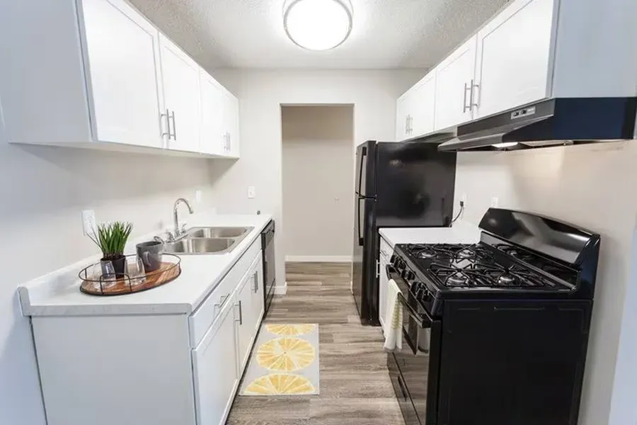 Narrow galley kitchen with white cabinets, black appliances, and gray flooring.